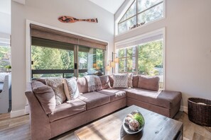 Ein modernes Wohnzimmer mit einer Eckcouch, einem Couchtisch mit Dekoration und großen Fenstern mit Blick ins Freie.