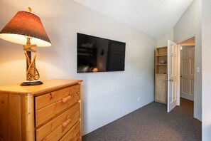 A room with a wooden dresser, a wall-mounted TV, and a door leading to another room. - Walk to Creekside Gondola | BBQ | Pets | Free parking (Whistler)