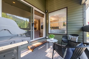 A covered outdoor seating area with a grill, a table with a potted plant, and a view into the house. - Walk to Creekside Gondola | BBQ | Pets | Free parking (Whistler)