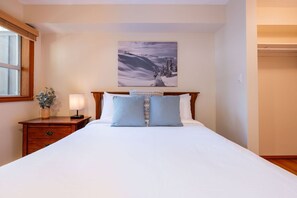 Ein ordentlich bezogenes Bett mit Kopfteil, ein Nachttisch mit Lampe, ein Fenster mit Ausblick und ein Bild an der Wand.