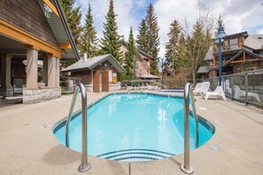 A swimming pool with a metal ladder, surrounded by lounge chairs and a wooden building with a sign. - Great location | Hot tub, pool & sauna | BBQ | AC (Whistler)