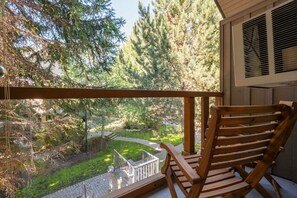 Ein hölzerner Schaukelstuhl auf einem Balkon mit Blick auf einen Garten, Bäume und einen Pfad.