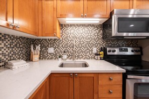 A kitchen with wooden cabinets, a stainless steel microwave, a black stove, and a tiled backsplash. - Great location | Hot tub, pool & sauna | BBQ | AC (Whistler)