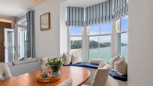Un comedor con una mesa de madera, sillas y vistas al mar a través de amplios ventanales.