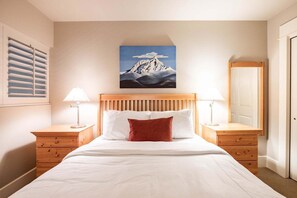 Ein Schlafzimmer mit einem Holzbett, weißer Bettwäsche, einem Bergbild an der Wand und zwei Nachttischen mit Lampen.