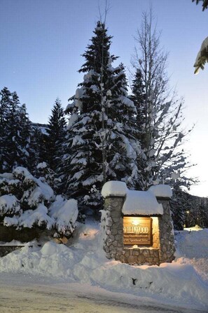 Ein Steinschild mit der Aufschrift 'Wildwood Lodge', umgeben von schneebedeckten Bäumen.