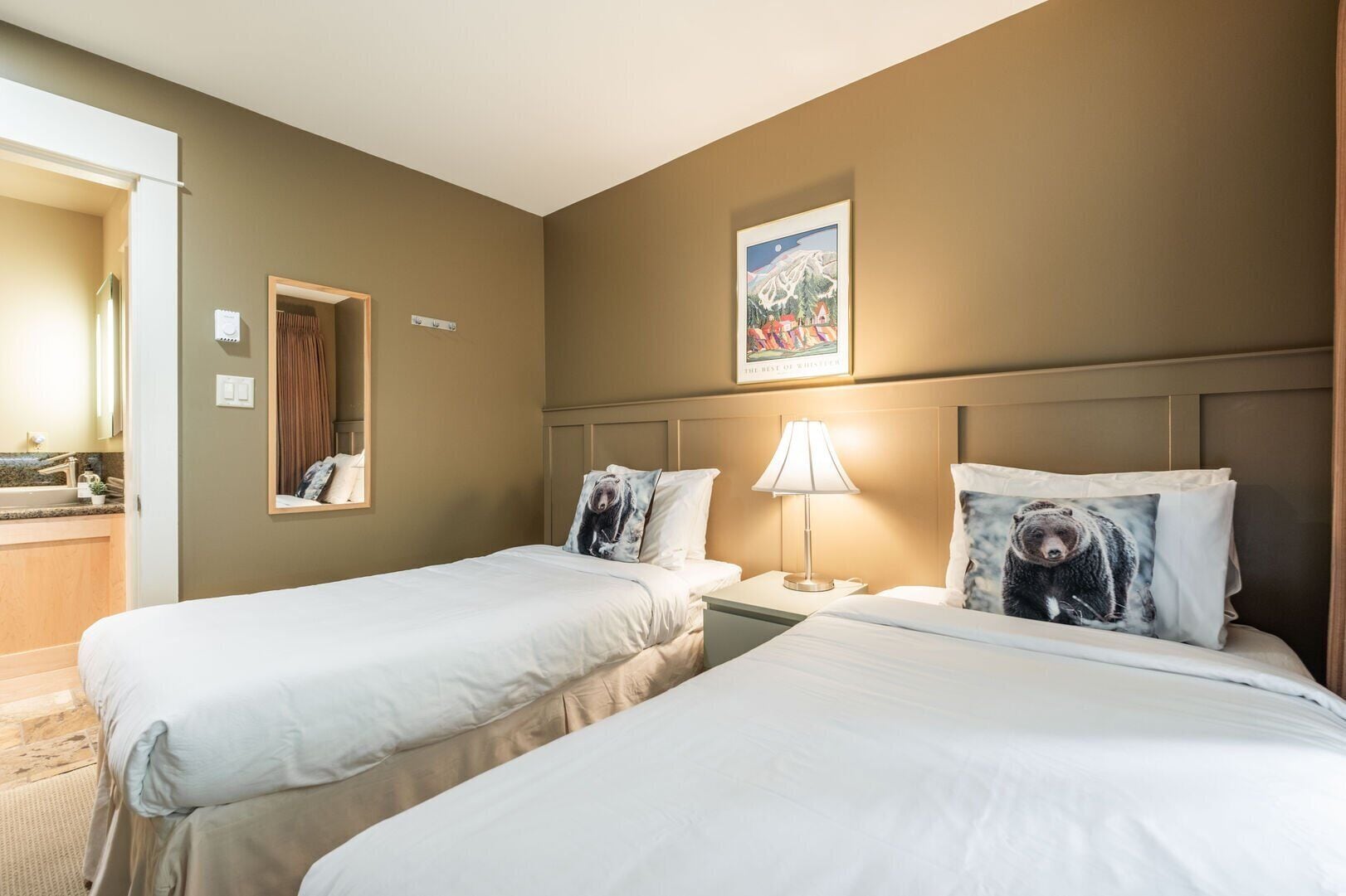 Een hotelkamer met twee bedden, een nachtkastje met een lamp, een spiegel en een schilderij aan de muur.