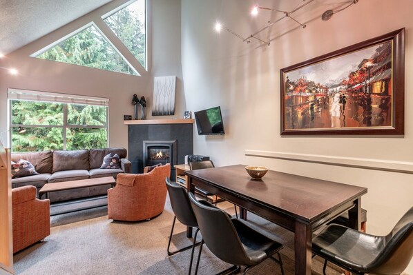 A modern living room with a fireplace, seating area, dining table, and artwork. - Free Parking | Steps to Blackcomb | Shared Hot Tub (Whistler)