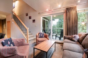 A living room with a staircase, two sofas, a coffee table, and a view of the outdoors through a glass door. - Free Parking | Steps to Blackcomb | Shared Hot Tub (Whistler)