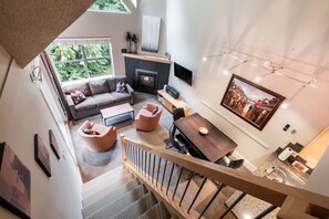 A modern living room with a fireplace, a dining area, and a staircase leading to an upper level. - Free Parking | Steps to Blackcomb | Shared Hot Tub (Whistler)