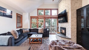 A living room with a sectional sofa, a coffee table, a fireplace, and a TV mounted on the wall. - Pet friendly | Hot tub | BBQ | Free parking (Whistler)