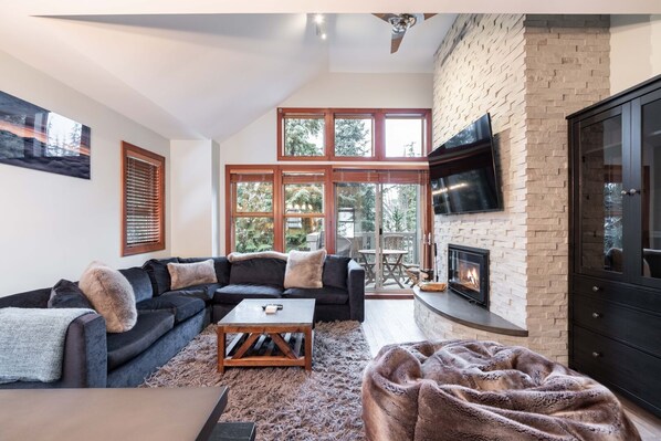 A living room with a sectional sofa, a coffee table, a fireplace, and a TV mounted on the wall. - Pet friendly | Hot tub | BBQ | Free parking (Whistler)