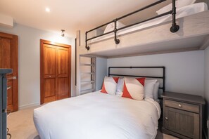 Una cama litera con estructura metálica, un armario de madera y una mesita de noche con cajones.