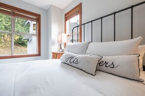 A bedroom with a bed, pillows, a nightstand, and a window with a view of trees and a building. - Pet friendly | Hot tub | BBQ | Free parking (Whistler)