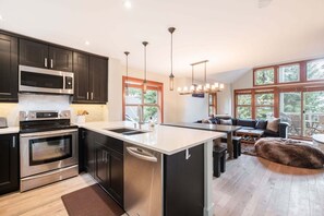 A modern kitchen with stainless steel appliances, a large island, and a dining area with a view of the outdoors. - Pet friendly | Hot tub | BBQ | Free parking (Whistler)