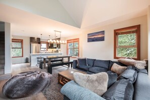A modern living room with a sectional sofa, a dining table, and a kitchen in the background. - Pet friendly | Hot tub | BBQ | Free parking (Whistler)