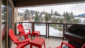 Ein Balkon mit roten Stühlen, einem Grill und Blick auf schneebedeckte Häuser und Bäume.