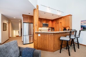 A modern kitchen with wooden cabinets, stainless steel appliances, and a bar area with stools. - Large deck with BBQ | Hot Tub | Golf Course (Whistler)