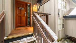 Eine Holztür mit einer kleinen Veranda, eine Holztreppe mit Schnee auf den Stufen und ein Fenster mit Fensterläden.
