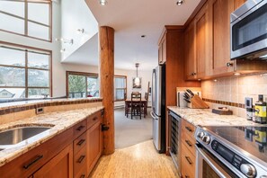 A modern kitchen with wooden cabinets, granite countertops, stainless steel appliances, and large windows. - Large deck with BBQ | Hot Tub | Golf Course (Whistler)