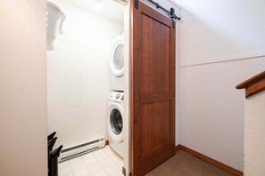 A laundry room with a wooden door, a washing machine, and a dryer. - Large deck with BBQ | Hot Tub | Golf Course (Whistler)