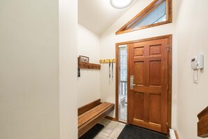 A hallway with a wooden bench, a door with a window, and a wall-mounted sign. - Large deck with BBQ | Hot Tub | Golf Course (Whistler)