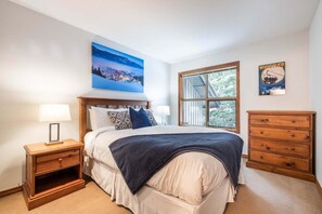 A bedroom with a bed, nightstands, a dresser, a window with a view, and a painting on the wall. - Large deck with BBQ | Hot Tub | Golf Course (Whistler)