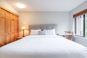 A bedroom with a large bed, wooden wardrobe, bedside lamp, and a window with a view. - BBQ | Free Parking | Spacious | Forest views (Whistler)