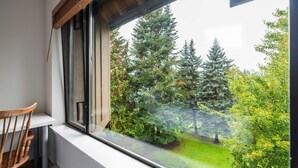 Ein Zimmer mit Fensterblick auf einen Garten mit Bäumen und Rasen.