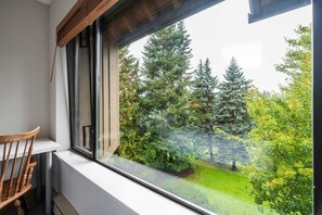 Ein Zimmer mit Fensterblick auf einen Garten mit Bäumen und Rasen.