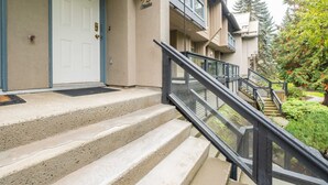 Ein Wohngebäude mit Hauseingang, einer Treppe zu einem Balkon und einem gepflegten Garten.