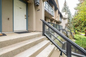 Ein Wohngebäude mit Hauseingang, einer Treppe zu einem Balkon und einem gepflegten Garten.