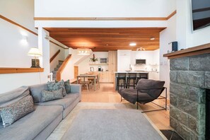 A cozy living room with a sofa, a fireplace, and a kitchen in the background. - BBQ | Free Parking | Spacious | Forest views (Whistler)