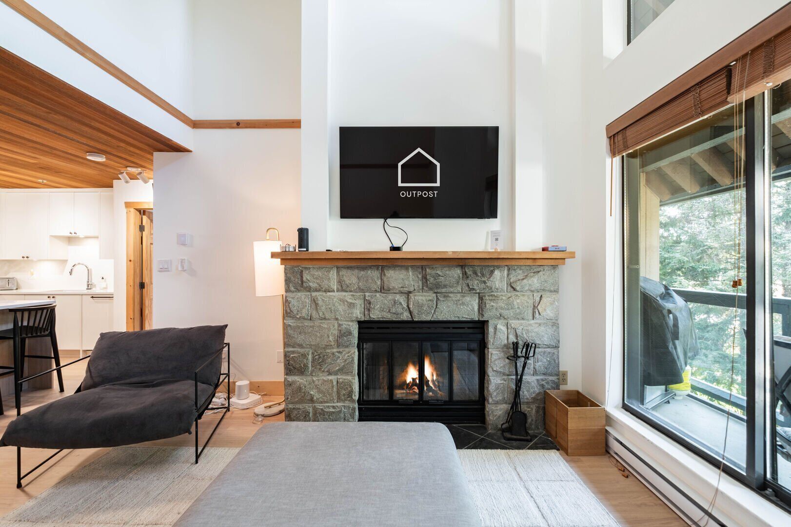 Una sala moderna con chimenea de piedra, un televisor de pantalla plana montado y un ventanal con vistas a árboles.