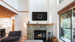 Ein modernes Wohnzimmer mit Kamin aus Stein, einem Wand-Fernseher und einem großen Fenster mit Blick ins Freie.