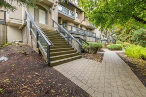 A multi-story building with a staircase leading to the entrance, surrounded by greenery and a paved walkway. - BBQ | Free Parking | Spacious | Forest views (Whistler)