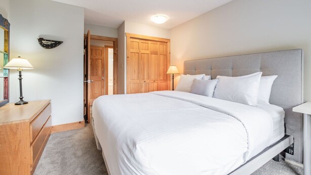 Ein Hotelzimmer mit einem großen Bett, zwei Nachttischlampen, einem Holzschrank und einer Tür zu einem weiteren Raum.
