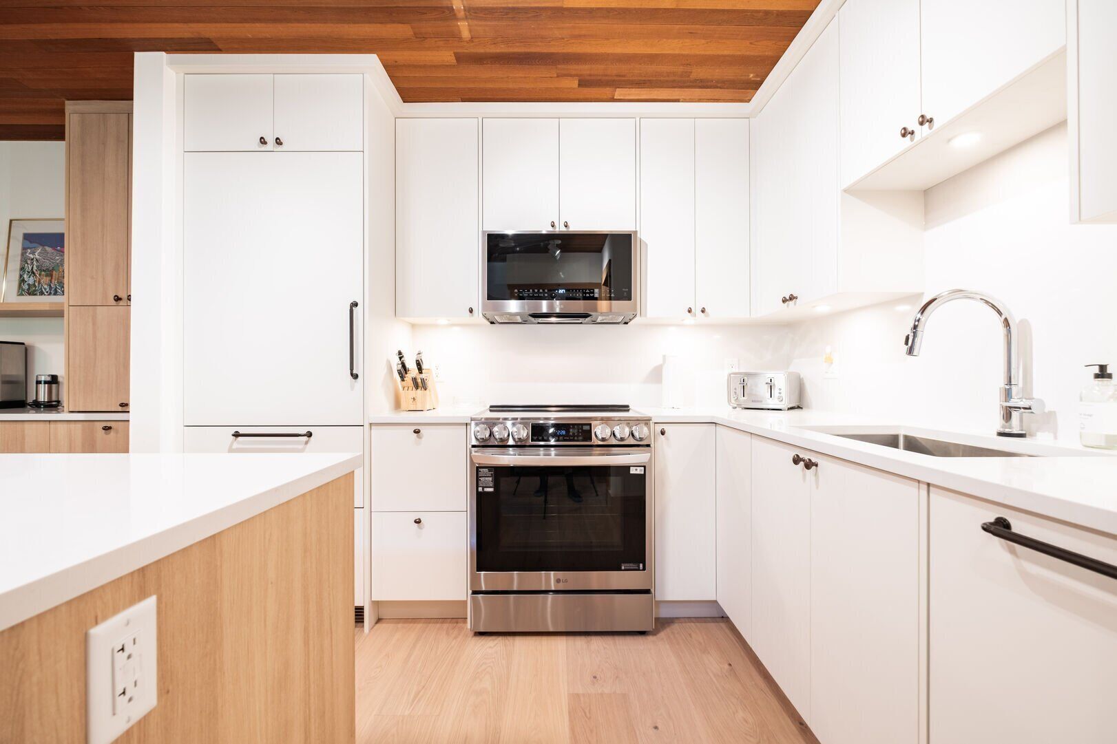 Una cocina moderna con armarios blancos, electrodomésticos de acero inoxidable y techo de madera.