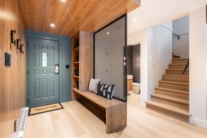 A modern interior with a wooden floor, a blue door, a bench with cushions, and a staircase. - Stunningly renovated | Walk to Blackcomb | Private Garage | Pets (Whistler)