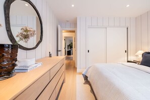 A modern bedroom with a wooden dresser, a large mirror, a bedside table with a lamp, and a bed with a white comforter. - Stunningly renovated | Walk to Blackcomb | Private Garage | Pets (Whistler)