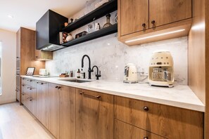 Eine moderne Küche mit Holzschränken, einem schwarzen Wasserhahn, einer weißen Kaffeemaschine und einer Marmorarbeitsplatte.