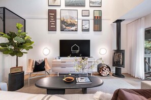 Ein modernes Wohnzimmer mit Kamin, einem an der Wand montierten Fernseher und einem Couchtisch mit Buch und Dekorationselementen.