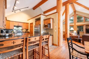 A spacious kitchen with wooden cabinets, a large island, and a dining area with chairs. - Private hot tub | Private garage | BBQ | Luxury (Whistler)