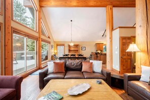 Ein gemütliches Wohnzimmer mit Ledersofa, Holzbalken, einem Essbereich und Blick durch große Fenster.