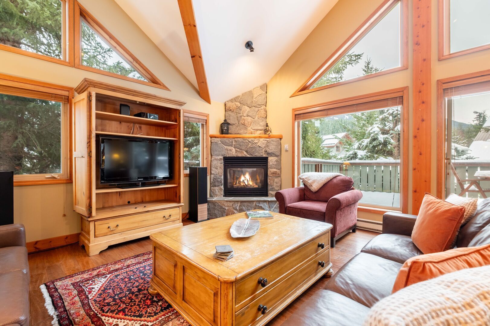 A cozy living room with a fireplace, wooden furniture, and large windows.