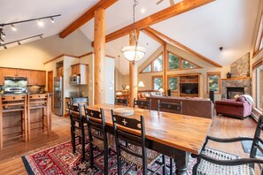 A spacious kitchen with wooden beams, a dining area with a large table and chairs, and a cozy living room with a fireplace. - Private hot tub | Private garage | BBQ | Luxury (Whistler)