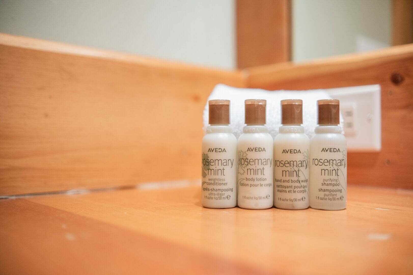Quatre bouteilles de shampoing à la menthe et au romarin de la marque Aveda, posées sur une surface en bois.