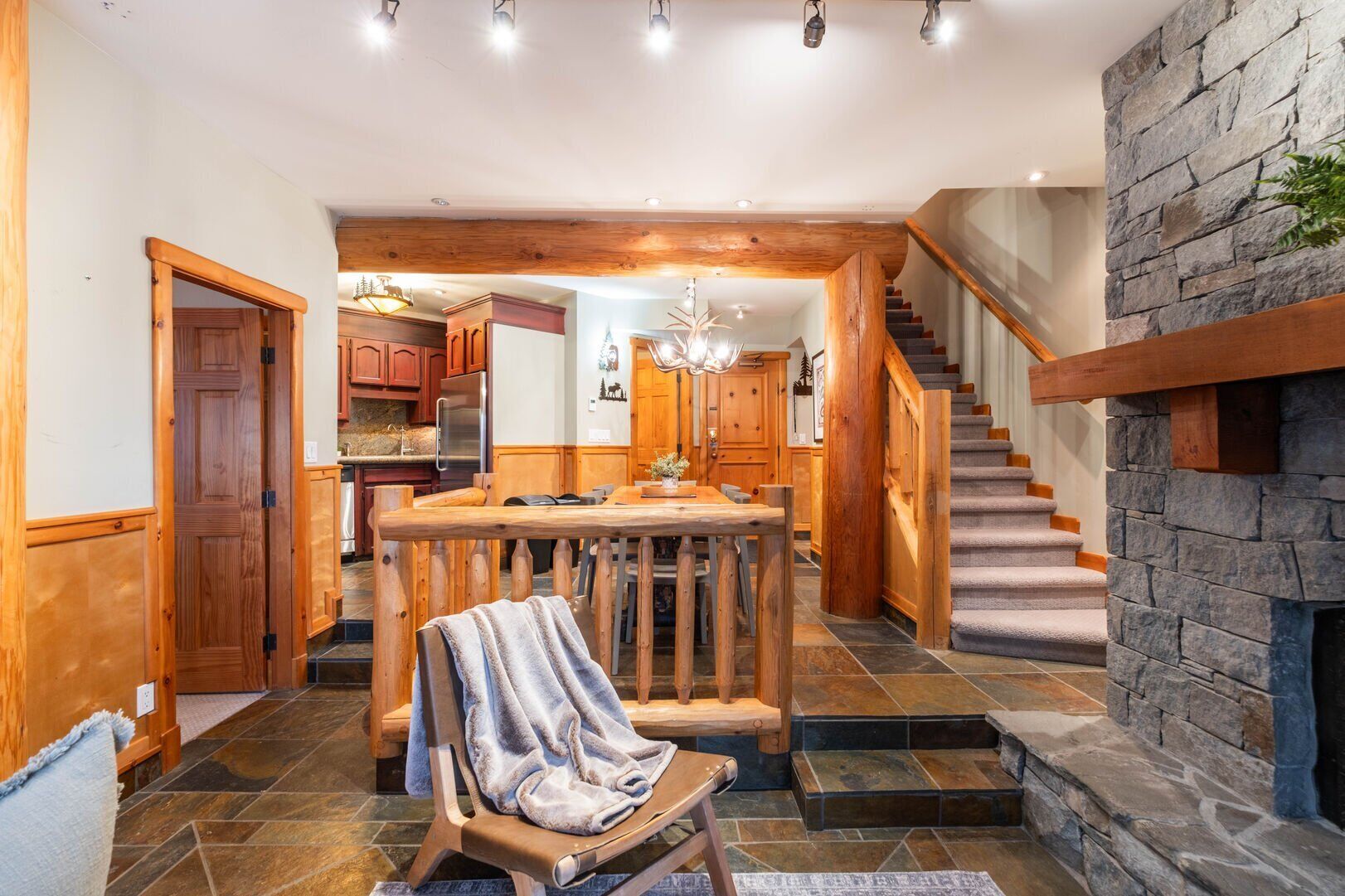 A spacious interior with a central wooden dining table, a stone fireplace, and a staircase leading to an upper level.