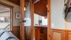 Et interiør i træ med en skydedør til et udendørs område, en polstret bænk og en vægmonteret lampe.
