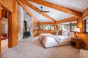 A cozy bedroom with a stone fireplace, a large bed, and a view of the outside. - Luxury log chalet | Private hot tub | Ski-in/out (Whistler)